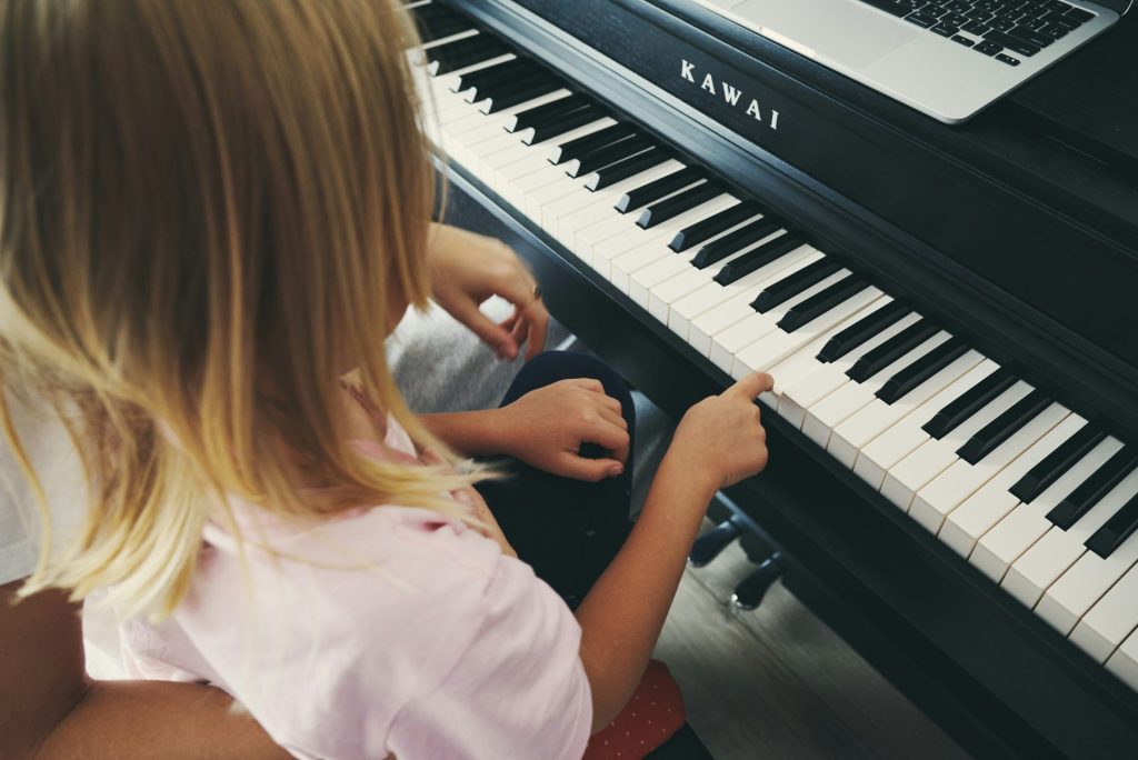 Young girl plays piano with laptop nearby